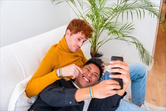 Beautiful gay couple being romantic indoors at home on the sofa, gay couple taking selfie, lgbt concept