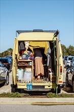 A yellow camper van with busy woman inside parked on a crowded parking lot in Portugal