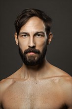 Portrait of topless serious man with beard and mustache looking straight severe