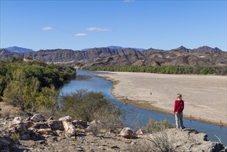 Woman standing on the Orange River, also known as the Orange River, on the border between Namibia and South Africa, Oranjemund, Sperrgebiet National Park, also known as Tsau ÇKhaeb National Park, Nam...