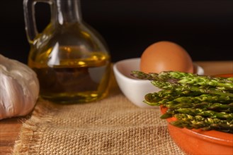 Close-up of wild asparagus in an earthenware casserole with olive oil, eggs and garlic black background