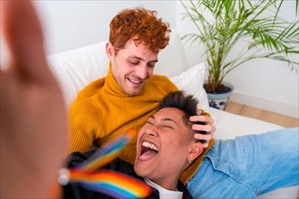 Beautiful gay couple being romantic indoors at home on the sofa, gay couple taking selfie laughing, lgbt concept