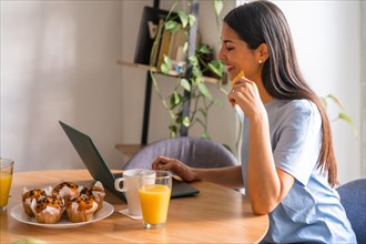 Woman shopping online with the computer while having breakfast in the morning by the window