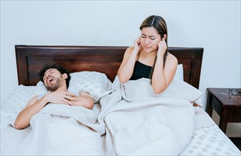 Husband snoring while the wife suffers and covers her ears. Sleep apnea concept, Snoring man in bedroom and wife covering her ears