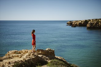 Attractive woman in red dress on top of cliffs at Sao Rafael Beach, Algarve coast, Portugal, Europe