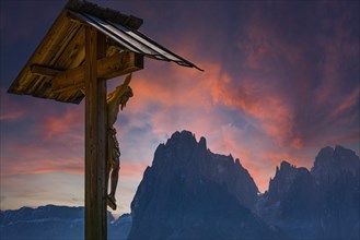 Wooden carved Christs Martyrdom, behind the peaks of the Sassolungo group in the sunset, Alpe di Siusi, Val Gardena, Dolomites, South Tyrol, Italy, Europe