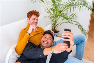 Beautiful gay couple being romantic indoors on the sofa, gay couple, taking a selfie