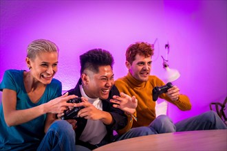 Group of young friends playing video games together on the sofa at home, purple led, having fun pushing