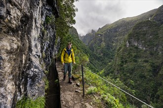 Hikers on a narrow path along a levada, view of forested mountains and gorges, Levada do Caldeirao Verde, Parque Florestal das Queimadas, Madeira, Portugal, Europe