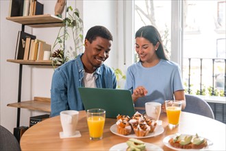 Multi-ethnic couple making online purchase with computer while having breakfast