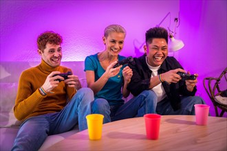 Group of young friends play video games together on the sofa at home, purple led