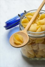 Conchiglie, shell pasta in glass container with cooking spoon, pasta