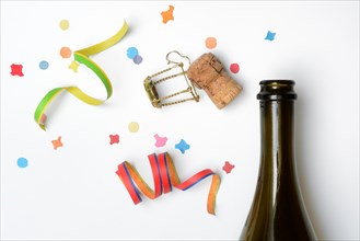 Champagne bottle, champagne cork, streamers and confetti against a white background