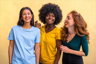 Portrait of beautiful multiethnic female friends smiling on a yellow wall