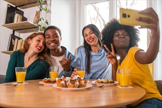 Multiethnic friends at a breakfast with orange juice and muffins at home, selfie smiling
