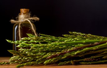 Bunch of fresh wild asparagus with a bottle of olive oil on a wooden table with black background