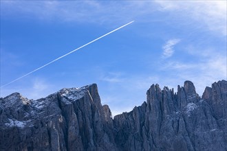 A jet plane with vapour trails flies over the peaks of the Latemar, Dolomites, South Tyrol, Italy, Europe