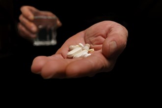 Man with pills in one hand and a glass of water in the other isolated on black background