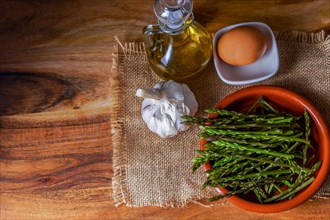 Top view of wild asparagus in clay pot on a burlap cloth with eggs, olive oil and garlic