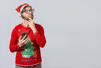 Handsome man in christmas clothes thoughtful holding cell phone. Thoughtful man with christmas hat holding cell phone, Young man in christmas clothes thoughtful with cell phone isolated
