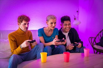 Group of young friends play video games together on the sofa at home