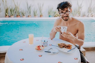 Breakfast near the swimming pool. Young man on vacation in hotel having breakfast near swimming pool. Person having breakfast in the hotel with pool in the background
