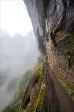 Hiker in the fog, Pico Arieiro to Pico Ruivo hike, hiking trail at rock cliff, Central Mountains of Madeira, Madeira, Portugal, Europe