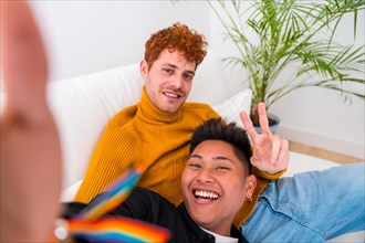 Beautiful gay couple being romantic indoors at home on the sofa, gay couple taking selfie, lgbt concept
