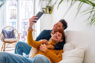 Beautiful gay couple being romantic at home on the sofa, taking a selfie, lgbt concept
