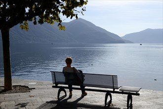 Bench with woman on the lakeshore of Ascona, Ticino, Switzerland, Europe