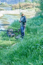 Male angler preparing on the river for a day of carpfishing, setting up the rods on the stand