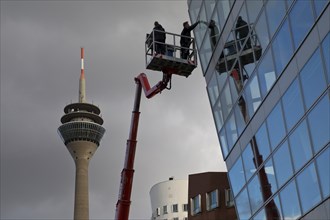 Building cleaner on a working platform with extended crane with Rhine Tower, Duesseldorf, North Rhine-Westphalia, Germany, Europe