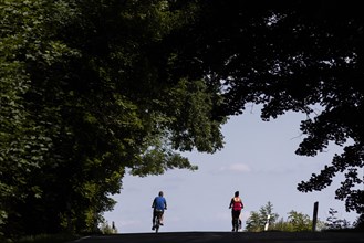 A man and a woman riding a bicycle on a country road in Pfaffendo, Pfaffendorf, Germany, Europe