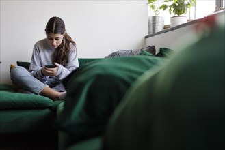 12 year old girl with a smartphone on the sofa, Bonn, Germany, Europe