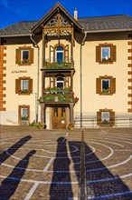 Circular pavement, behind it an older house in Ladin style, with balconies decorated with flowers, Sankt Christina, Val Gardena, Dolomites, South Tyrol, Italy, Europe