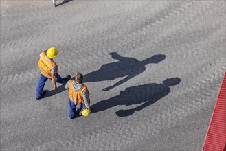 Construction workers with hard hats walking on a street, casting a shadow, Stuttgart main station, Baden-Wuerttemberg, Germany, Europe