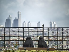 Two woman in burqas on a park bench in front of the modern skyline of Istanbul Istanbul, Turkeyio