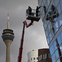 Building cleaner on a working platform with extended crane with Rhine Tower, Duesseldorf, North Rhine-Westphalia, Germany, Europe