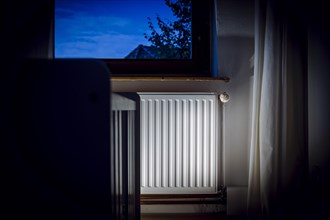 Symbolic photo on the subject of rising heating costs for gas heating. A heater is illuminated in a room during twilight. Berlin, Berlin, Germany, Europe