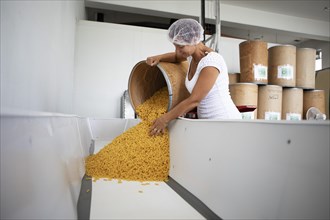 Woman with hair protection tipping noodles from a storage bin into a tub, Finkensteiner Nudelfabrik, Finkenstein am Faaker See, Villach region, Carinthia, Austria, Europe