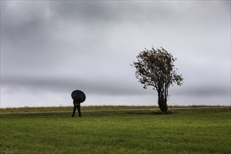 Man with umbrella in the rain in strong wind on a ridge in the Eifel borderland of Germany and Belgium, province of Liege, Belgium, Europe