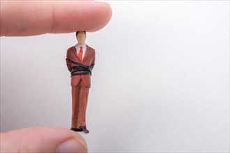 Hand holding tiny figurine of man model tied in a rope