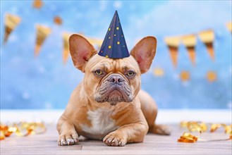 French Bulldog with birthday part hat in front of blurry blue background with garlands and party streamers