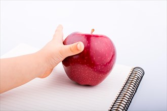 Hand holding a red apple on a notebook a white background