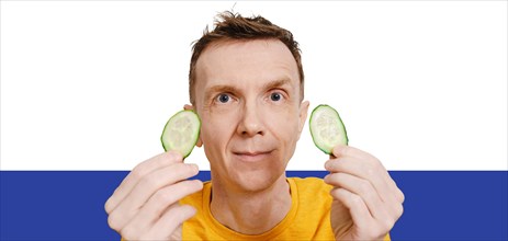 Middle-aged man holds two slices of cucumber in hands