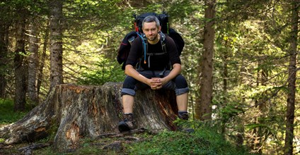 A man sitting with a backpack on a tree trunk by the trail. Dolomites