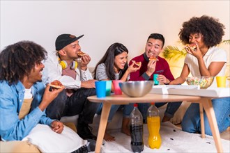 Group of multiethnic friends on a sofa eating pizza and drinking soda at a home party