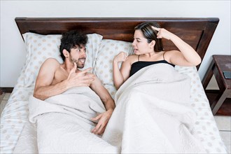 Upset couple lying in bed arguing. Top view of young couple lying in bed arguing. Marriage problems concept