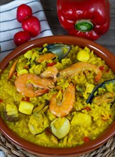 Portion of typical spanish seafood paella in a clay casserole with all its ingredients