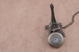Little model Eiffel Tower and a pocket watch on brown background